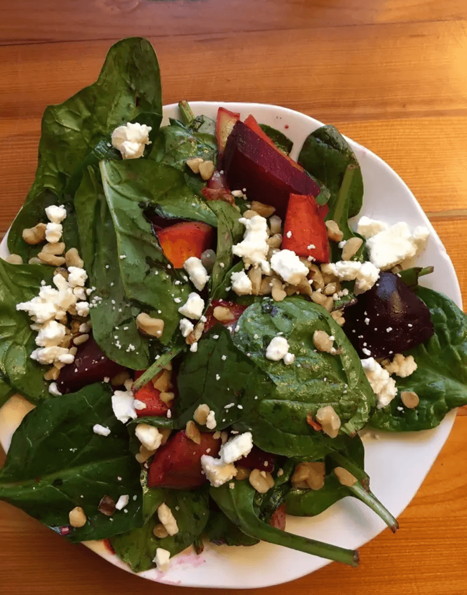 Overhead view of Balthazar beet salad—roasted beets, baby spinach, crumbled feta, and walnuts on a white plate